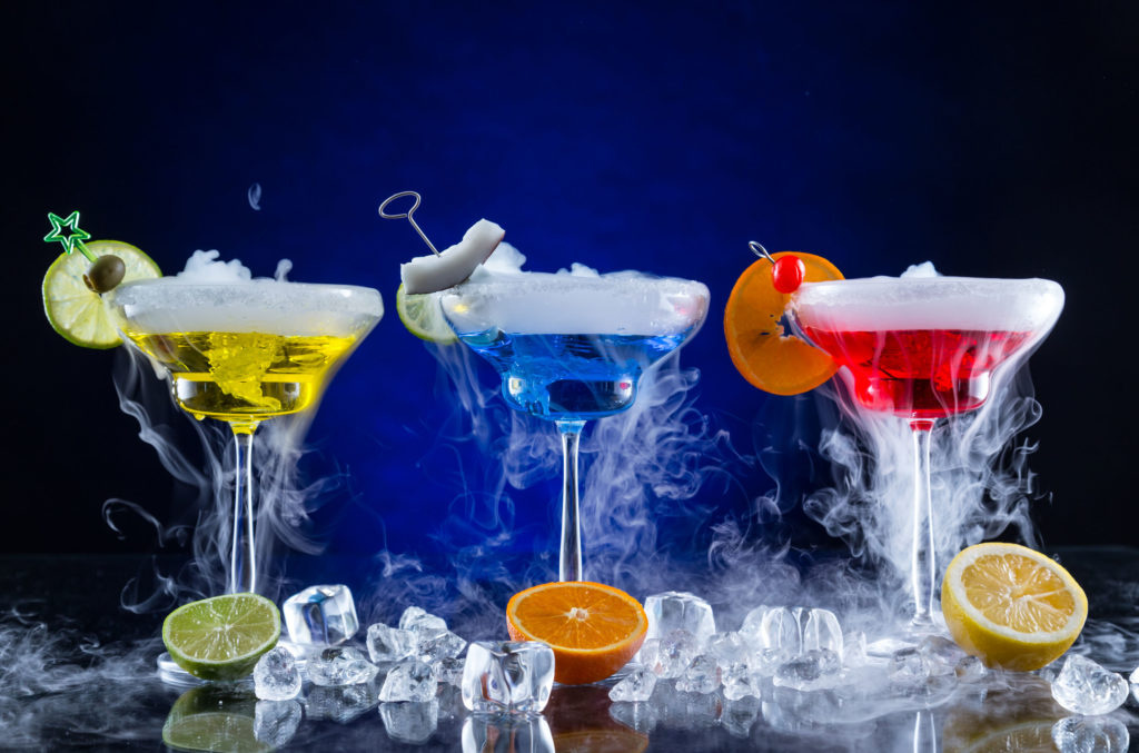 Martini drinks with dry ice smoke effect, served on bar counter with dark colored background